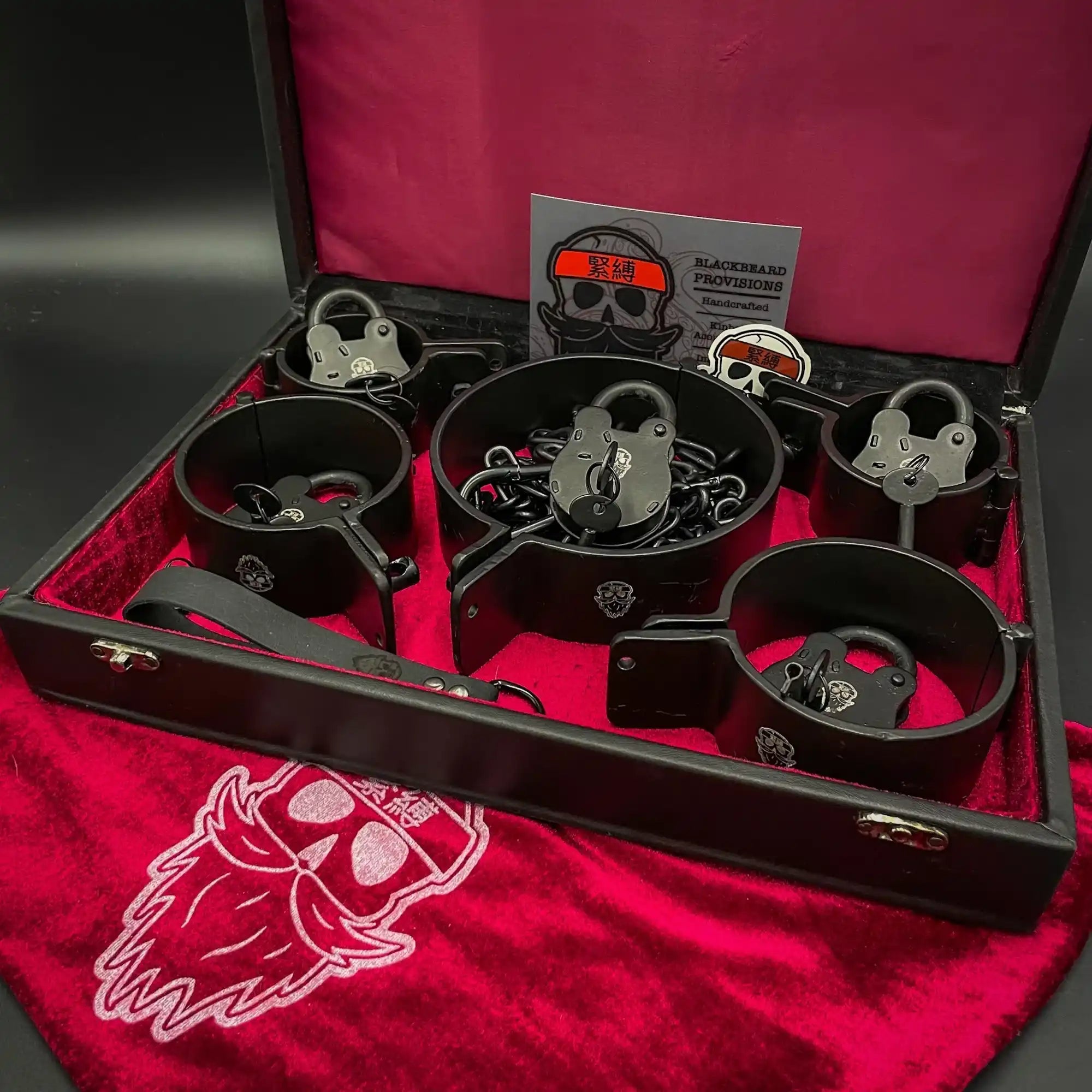 Collection of metal restraints or shackles displayed in a wooden case with red velvet lining.