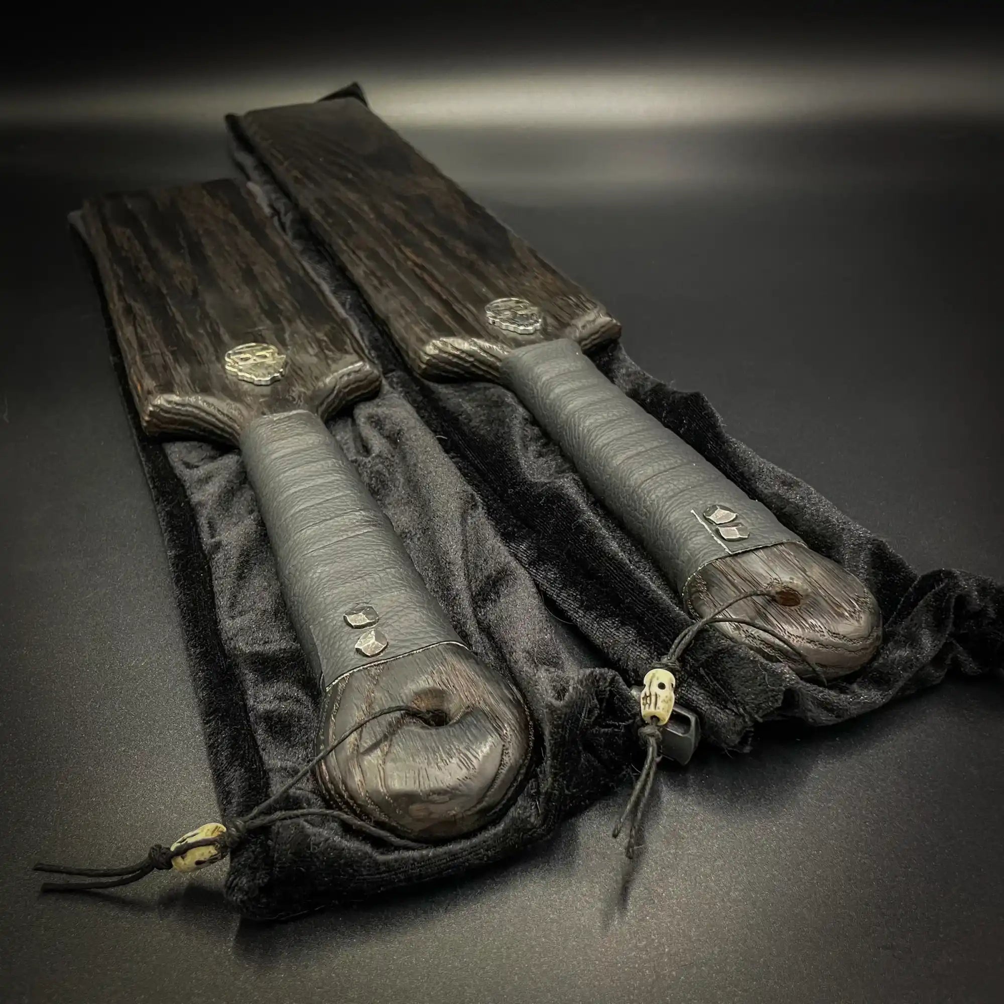 Two black leather sword sheaths with decorative metal fittings and tassels.